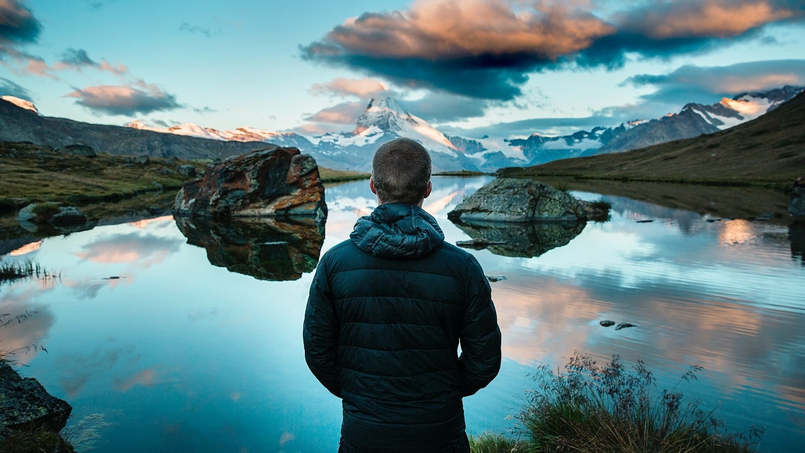 man standing in front view of lake surrounded with mountains